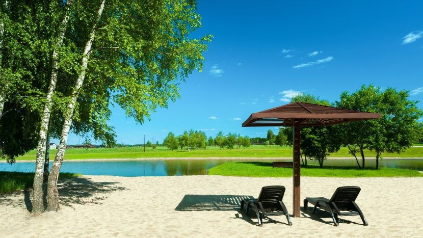 Песчаный пляж с навесом и шезлонгами на берегу собственного озера в Green Forest Park